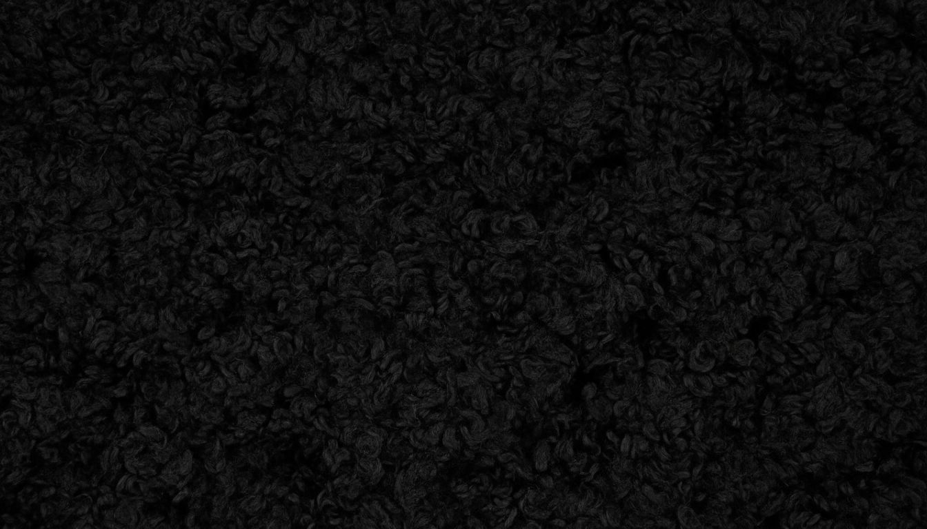 Крупный план текстуры мелко завитого искусственного каракуля глубокого матового черного цвета.